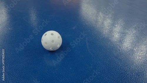 White floorball ball rolls across blue arena floor, showcasing continuous motion and dynamic positioning in a sports setting