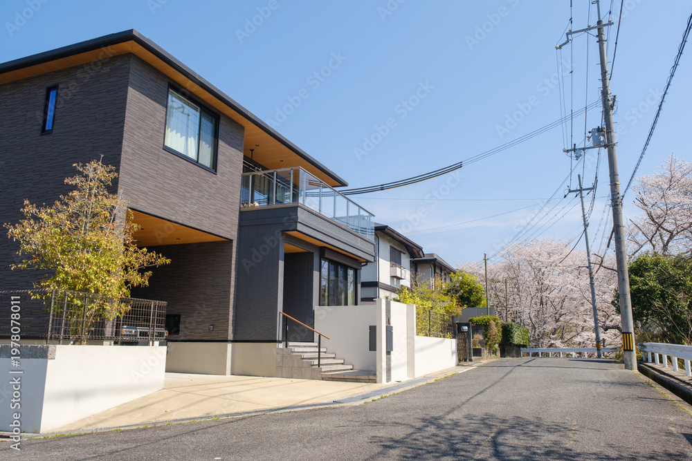 Obraz premium 桜が咲く街並みに佇むモダンな注文住宅：春の青空と理想の一戸建てマイホーム