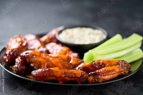 crunchy buffalo chicken wings with celery sticks and blue cheese dipping sauce on a dark table.