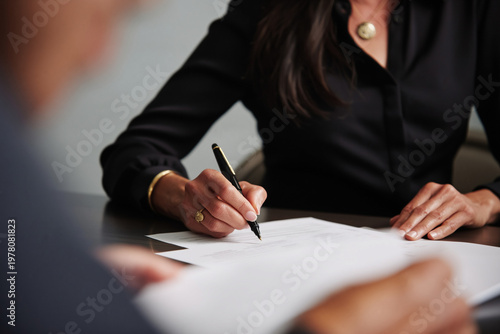 Professional businesswoman signing an important document with a pen at a dark desk in a modern office