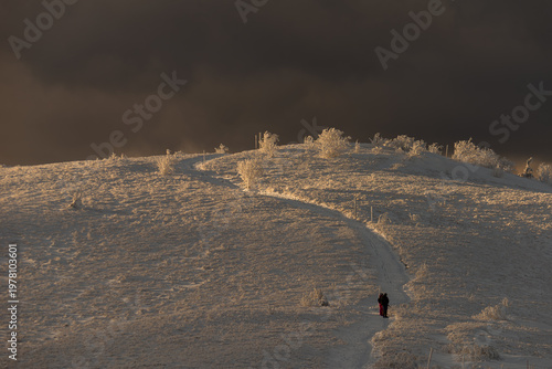 Dramatic winter mountain landscape in Bieszczady with dark storm clouds gathering over snow-covered peaks during twilight.