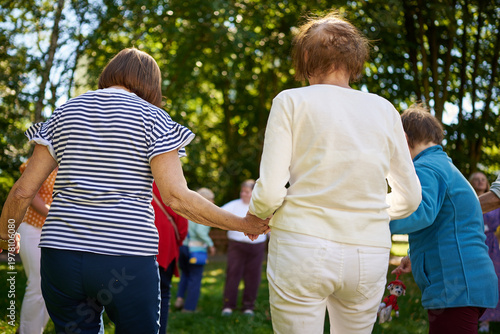 Group of elderly people holding hands while standing in a circle during an outdoor activity, care home garden, Warszawa, Masovian Voivodeship, Poland, Europe.