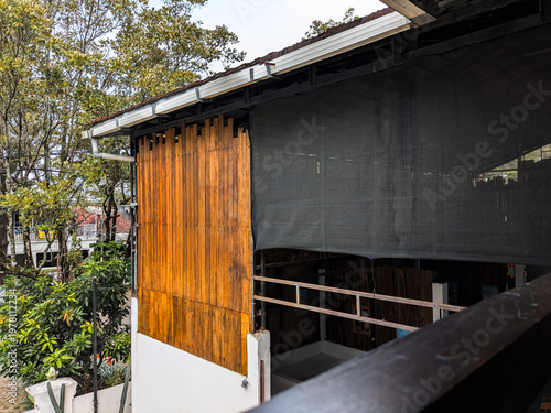 Restaurant exterior with vertical wooden signage panel, shaded terrace, and surrounding trees in a cozy outdoor dining setting.
