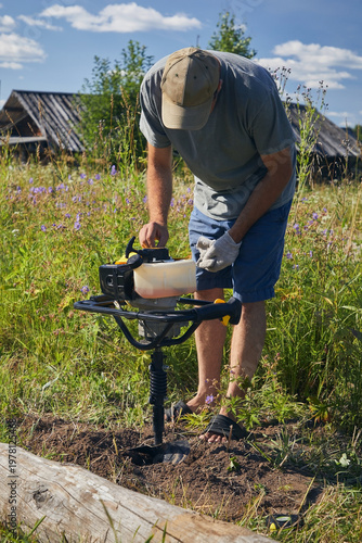 A man drills holes for a fence with a gas-powered auger