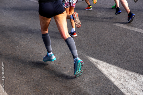 Female runner in legs compression socks running in group of athletes
