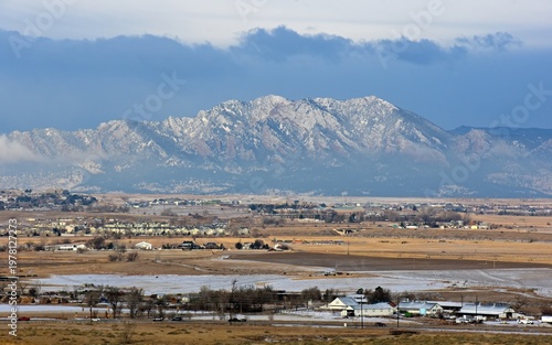 the  striking boulder flatirons and  snow -capped peaks of the front range of the colorado rocky mountains in  spring, with dramatic clouds and farm houses,  as seen from broomfield, colorado, in earl