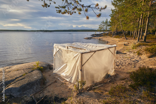 A homemade sauna made of film on the sandy shore of a lake