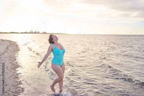 plus size woman in a turquoise swimsuit splashing in the sea on a Copenhagen beach