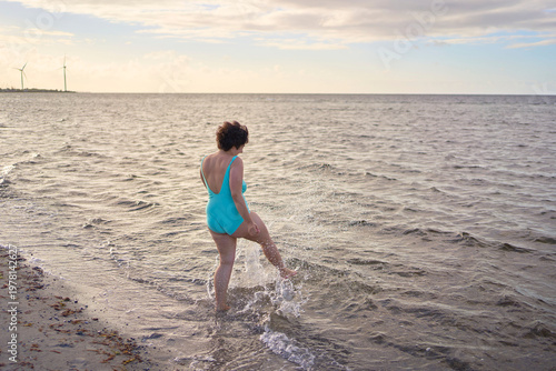 plus size woman in a turquoise swimsuit splashing in the sea on a Copenhagen beach