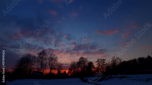 Silhouettes of trees and houses in a town at night, by the end of the day in bold sunset sky.
