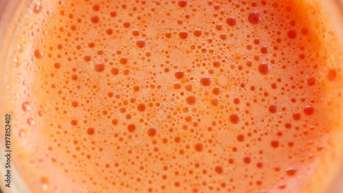 Extreme close up of fresh orange juice surface with bubbles and foam texture