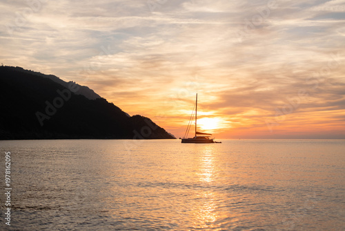 Sailing boat floating in the harbor around Corsica Island during sunset while the sky turns from blue to golden.