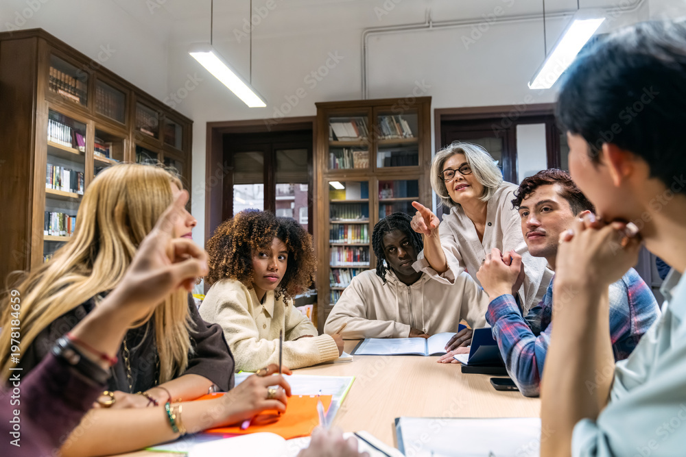 Obraz premium Group of diverse college students actively participating in a study session, discussing topics with a female professor in a library setting