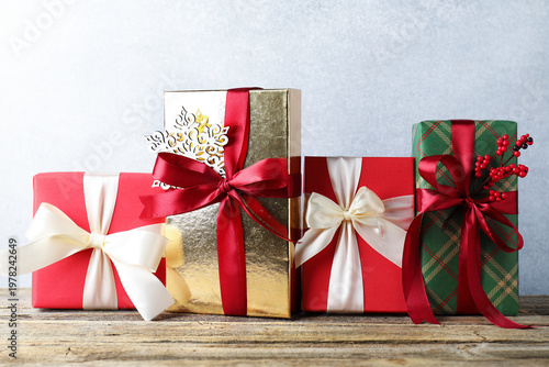 Many gift boxes with decor on wooden table near grey wall, closeup. Merry Christmas and Happy New Year