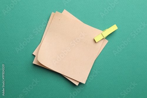 Blank paper notes with clothespin on green background, top view