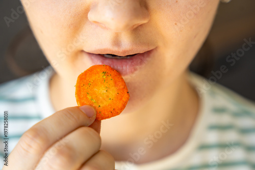 Woman eating carrot chip as healthy snack at home. Clean eating and mindful diet concept with natural vegetable chips.