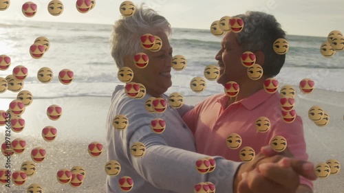 Senior couple holding hands, dancing on beach, emoji cascade starting from left for marketing