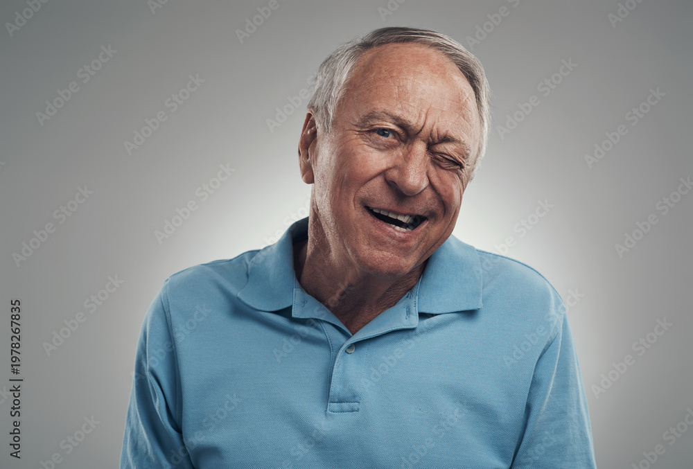 Obraz premium Portrait, wink and old man in studio with smile, playful gesture and funny personality for retirement. Happy, elderly person and blink eye with confidence, humor and good mood on white background.