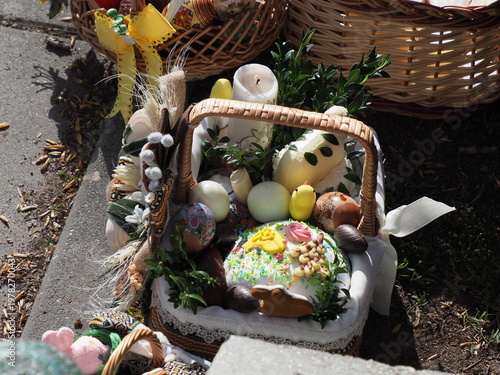 Detailed view of a traditional Easter basket with bread, eggs and a white candle outdoors
