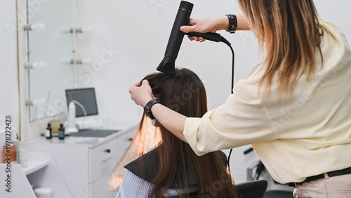 Foto A hairdresser blow-dries a client's long, natural, dark hair with a round brush and a styler at a salon