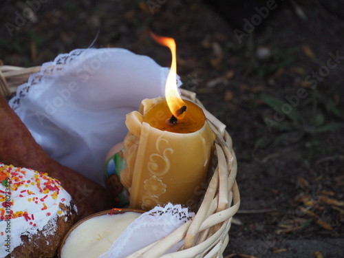 Lit candle in wicker basket with traditional Easter cakes and eggs in sunlight outdoors
