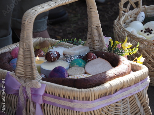 Traditional Easter basket with sausage, bread, and colored eggs decorated with purple ribbon during blessing.