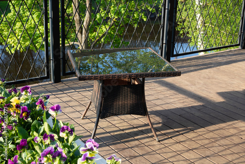 In the cafe on the veranda above the river, there is a table with a glass surface that reflects the blue sky and green trees.