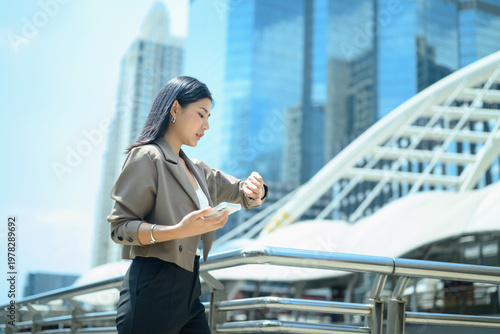 Fotografie Adult businesswoman standing on an urban walkway, checking her smartwatch rush h