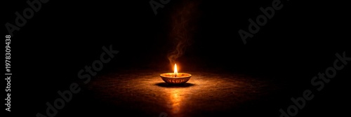 Single oil lamp for Indian Diwali festival glowing in darkness, spiritual celebration and light concept, wide banner with copy space.