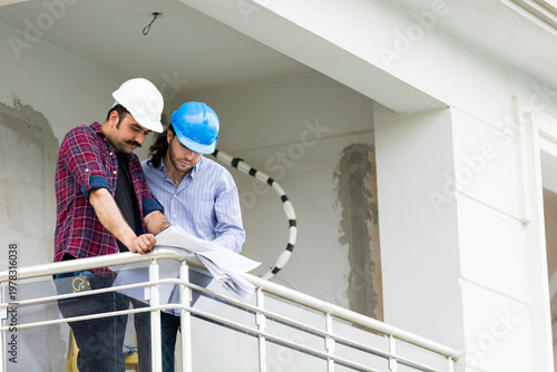 Two construction professionals or architects in hard hats looking at the horizon and discussing a project from a building balcony.