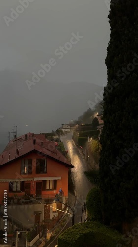 Rainy storm over Lake Como with lightning. Wet narrow slippery road, lakeside houses and dramatic dark sky create a cinematic moody atmosphere in northern Italy.