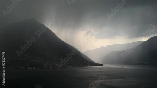 Storm over Lake Como with dark clouds, heavy rain and black water surface. Mountains covered in dense fog create a dramatic cinematic atmosphere over the Italian lake.