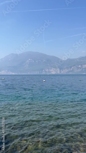 Panoramic view of Lake Garda with the Alps in the background, wooden pier and gently rippling water. Scenic Italian lakeside landscape.