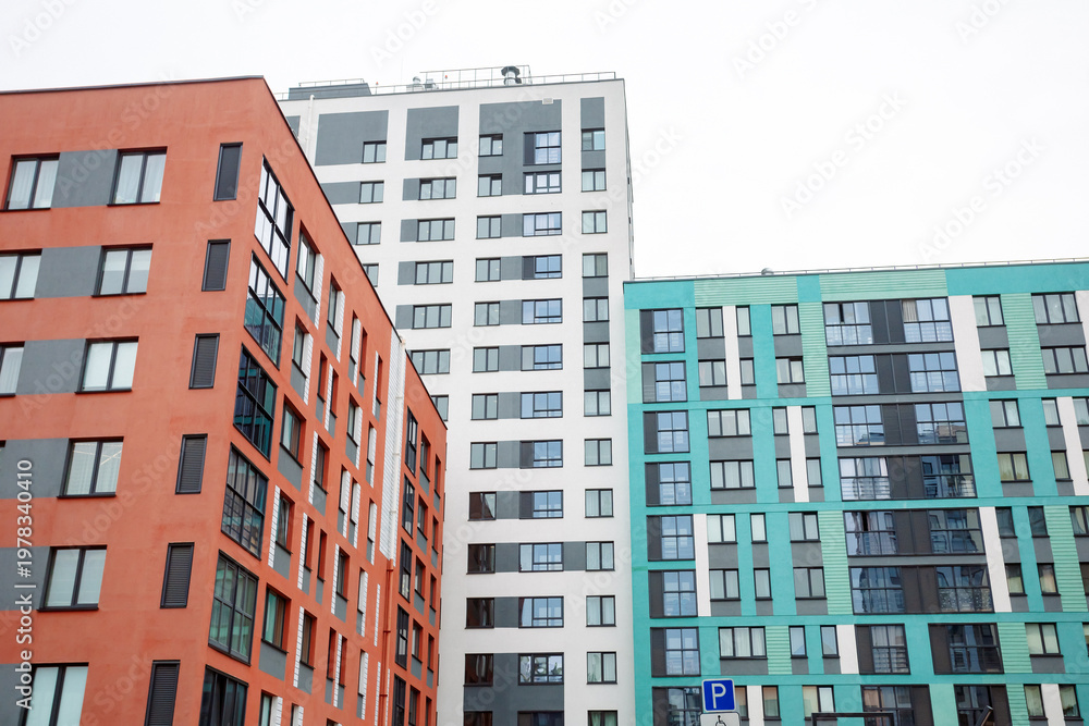 Fototapeta premium Modern apartment blocks stand tall and close. Bright colors contrast against grey skies. Windows reflect sunlight and city life. Urban development shapes cityscapes. Ideal for real estate