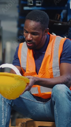 Tired and worried worker in a safety vest and hard hat, sitting with his head in his hands, logistics staff in a stressed workplace.
