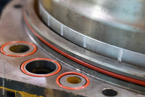 Photography Close up of orange rubber O-ring seals installed on a heavy industrial metal flange during a machinery maintenance and assembly process in a workshop for leak prevention