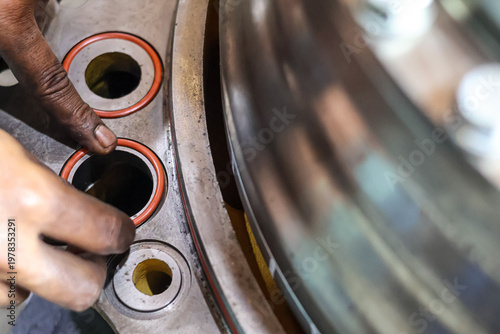 Obraz na płótnie Close up of a mechanic installing orange rubber O-ring seals into a heavy metal industrial engine component in a workshop during a professional machinery maintenance