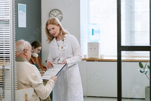Tableau sur toile Caucasian female doctor explaining medical form to senior male patient in clinic, supporting informed care and treatment decisions