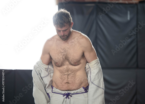 Man in jiujitsu gi kimono gym training, taking off the go, muscular but average dad bod.
