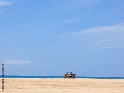 A large beach (Boa Vista Island, Cape Verde). An anonymous fisherman with his gear and a parked quad bike can be seen. Day, almost clear.
