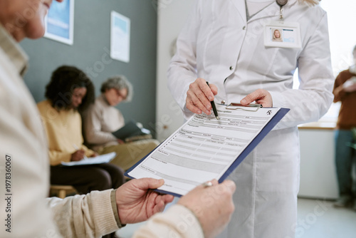 Photos Senior patient receiving medical intake form from female doctor in clinic, completing registration before appointment
