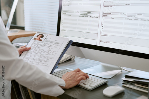 Fotografie Middle aged healthcare worker reviewing patient file and entering medical data i