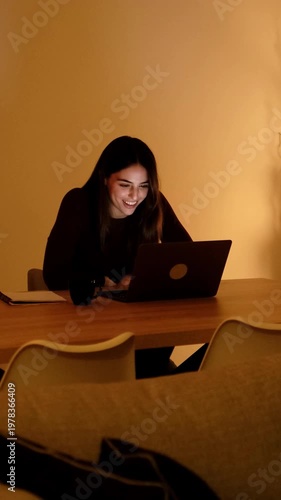 Young Woman Laughing and Smiling While Engaged with Her Laptop at Home in the Evening