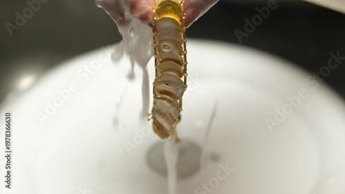 Goldsmith rinsing gold jewelry under running water after cleaning process. Shows goldsmithing workflow, surface purification and final preparation stage in traditional jewelry workshop.