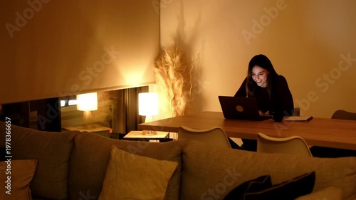Happy Young Woman Smiling While Working or Connecting on Laptop at Home in the Evening