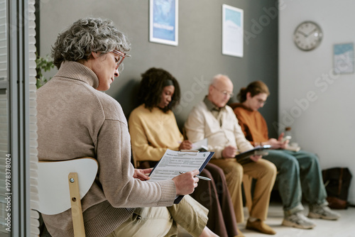 Photos Senior Caucasian woman reviewing intake form in clinic waiting room while divers