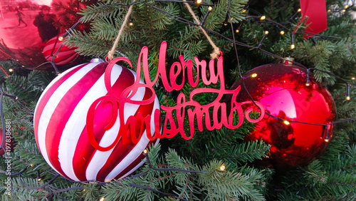 close up of merry christmas text sign on decorated tree with red and white striped baubles and twinkling lights