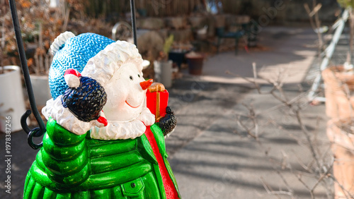 close up of a cute snowman figurine wearing green jacket and blue hat holding candy cane and red gift box for christmas decoration