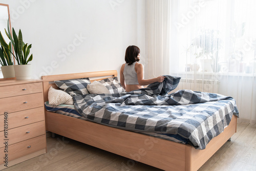 Fotografia Woman sitting up in bed in a bright bedroom, starting the morning and looking towards the daylight from the window