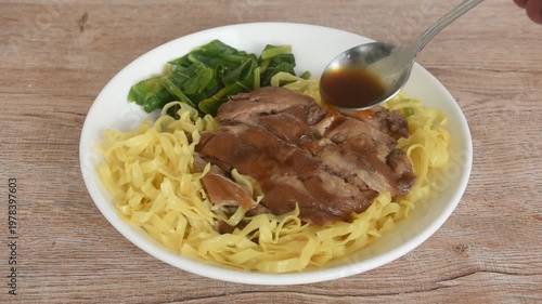 Chinese yellow egg nodles topping braised slice pork leg stew dressing black herb soup couple pickled cabbage and kale dipping spicy sour chili sauce on plate